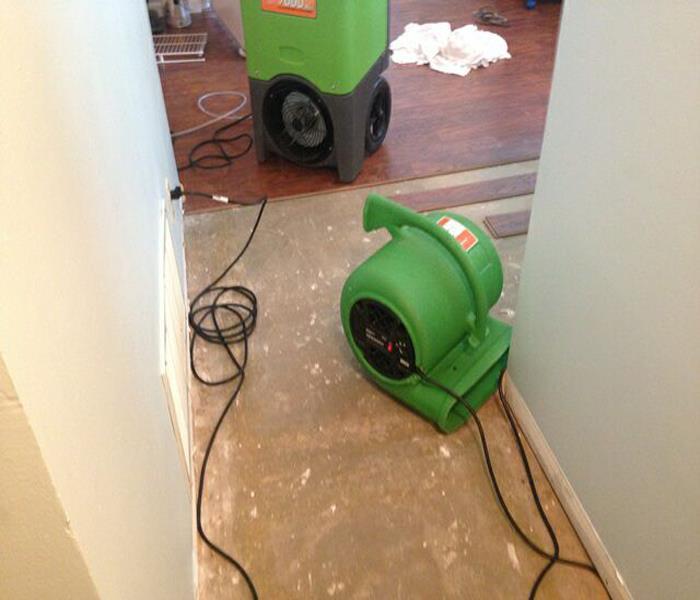 Image shows green SERVPRO fan and dehumidifier in a hallway where wood laminate flooring has been removed.