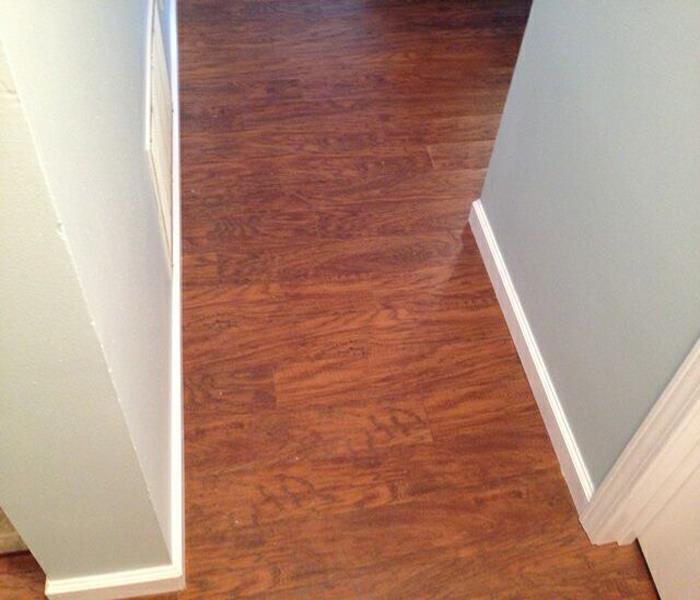 Image shows wood laminate flooring through a hallway with gray walls and white base trim.