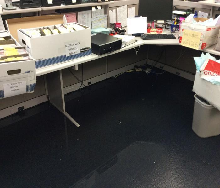 Image shows cubicle desk with water on the carpet underneath, items pilled up on the desk and out of the water.
