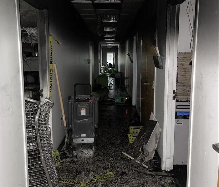 Image shows a hallway black with soot with SERVPRO equipment along the floor.